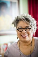 Photo of Lorraine Hansberry Literary Trust executive director, Joi Gresham, who sits in front of a portrait of Hansberry painted by Gladys Schwarz.